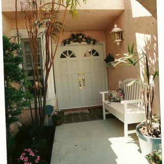 A charming front porch with a white double door, surrounded by potted plants and a cozy bench.