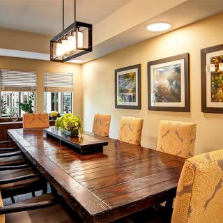 A cozy dining room with a large wooden table, upholstered chairs, and elegant lighting.