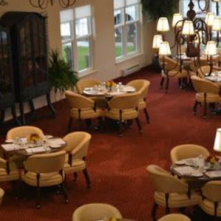 An elegant restaurant dining area with neatly arranged tables and chairs, featuring a warm carpeted floor and ambient lighting.