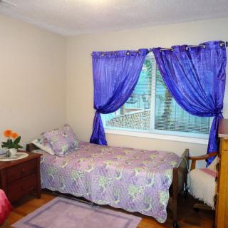 A cozy bedroom with a single bed, adorned with floral bedding and purple curtains.