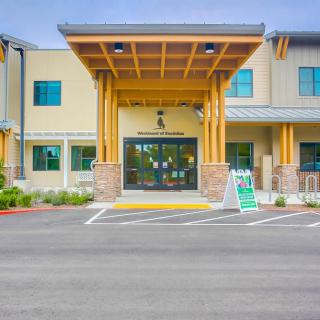 Front entrance of a modern building with wooden accents and a parking area.