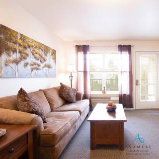 A cozy living room with a brown sofa, a wooden coffee table, and a large window allowing natural light.