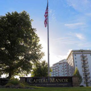 A view of Capital Manor, featuring the American flag against a backdrop of sunlight and residential buildings.