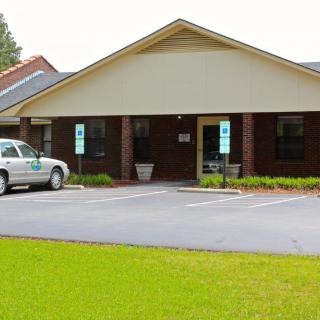 A small brick office building with a car parked in front and a well-maintained lawn.