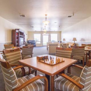 A cozy living room with a chessboard on the table surrounded by striped chairs and a bookshelf in the background.