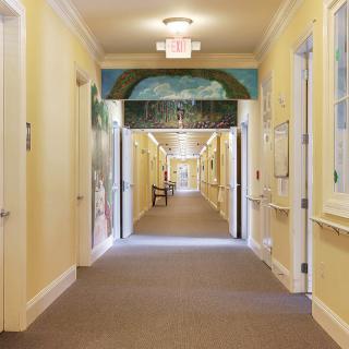 A brightly lit indoor hallway with doors lining both sides and a carpeted floor.