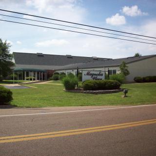 A building with a visible sign, situated alongside a road with greenery and a clear sky.
