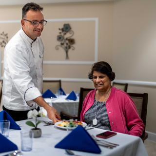 A chef serves a meal to a customer in a restaurant with elegant table settings.