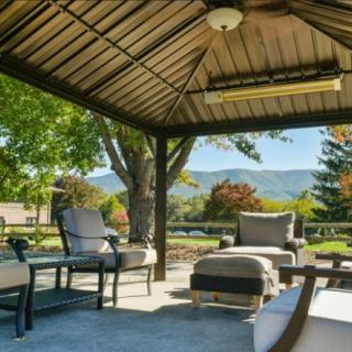 A cozy outdoor patio with comfortable seating under a gazebo, surrounded by trees and mountains.