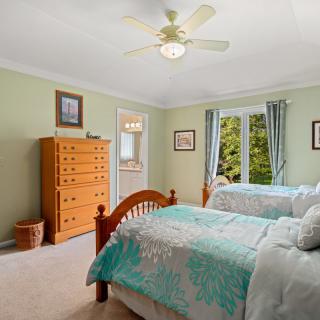 A cozy bedroom featuring twin beds with floral bedding, a wooden dresser, and a ceiling fan.