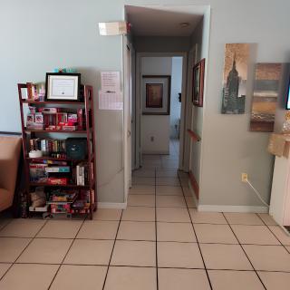 A view of a waiting room with a hallway, featuring a bookshelf and artwork on the walls.