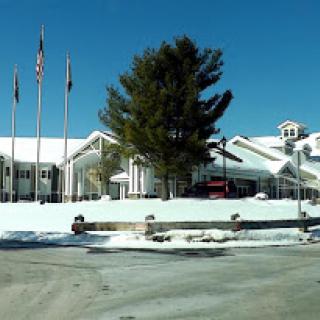 A hotel building blanketed in snow with flags and trees in front, under a clear blue sky.