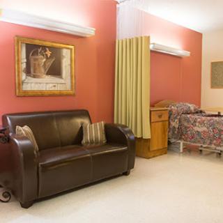 A cozy room featuring a brown sofa, a bed with floral bedding, and tasteful artwork on the walls.