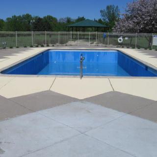 An outdoor swimming pool on a clear day, surrounded by trees and open space.