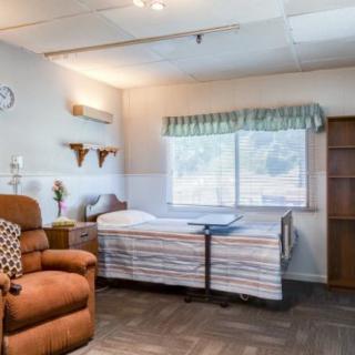 A hospital room featuring a patient bed, a recliner chair, and a window providing natural light.