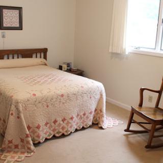 A cozy and minimalist bedroom featuring a bed with a decorative blanket and a rocking chair by the window.