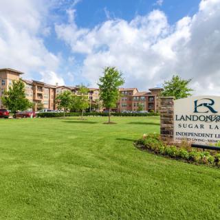 A scenic view of an apartment complex with a well-maintained lawn and a clear blue sky.