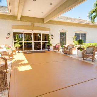 A sunny outdoor patio with wicker furniture and plants leading to a building entrance.
