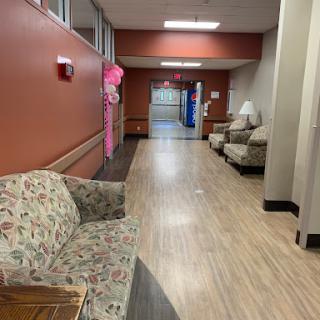 A quiet corridor featuring a seating area with floral-patterned chairs, leading to a door at the end.