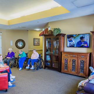 A group of elderly people in wheelchairs watching television in a communal living room.