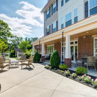A sunny outdoor patio area with furniture and landscaped garden in front of a multi-story building.