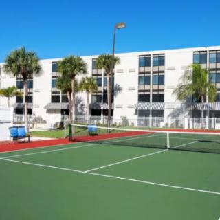 A well-maintained tennis court beside a residential building with palm trees on a sunny day.