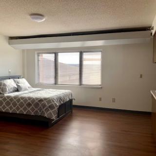A spacious bedroom with a bed, large window, and hardwood flooring.