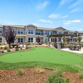 A modern residential building with a well-maintained garden and a mini golf area under a clear blue sky.