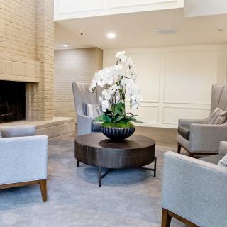 A modern lobby featuring comfortable seating around a fireplace, with a central coffee table adorned with an orchid plant.