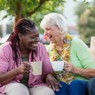Two elderly women enjoying coffee and conversation outdoors.
