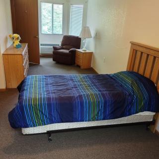 A cozy bedroom with a single bed, chair, and dresser, featuring a bright window.