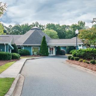 A view of a building with a circular driveway, surrounded by trees and landscaped gardens under a cloudy sky.