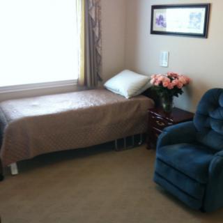 A cozy bedroom with a single bed, upholstered chair, and flowers on the nightstand.