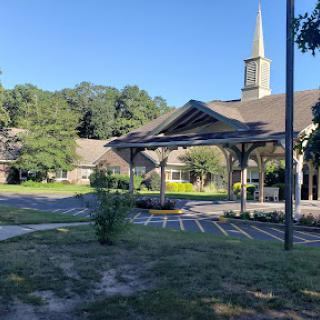 A peaceful view of a church building surrounded by greenery and blue skies.