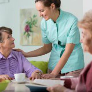 A caregiver interacts with elderly individuals in a care home setting.