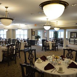 An elegant dining room with round tables set for service, featuring chandeliers and classic decor.