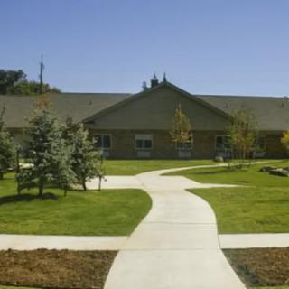 A building with a landscaped front yard, featuring a concrete pathway and surrounding trees.