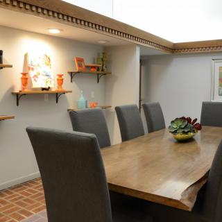 A modern dining room with a wooden table and gray chairs, featuring decorative shelves on the wall.