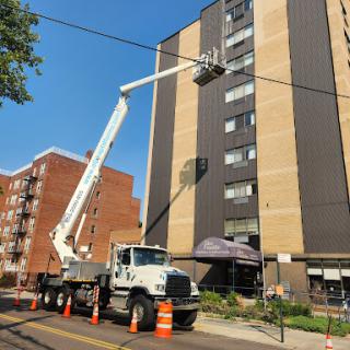 A bucket truck positioned in front of a multi-story building, used for maintenance work.