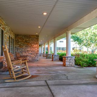 A peaceful porch with a wooden rocking chair, surrounded by columns and a lush garden.