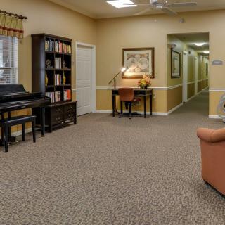 A cozy living room interior featuring a piano, bookshelf, and comfortable seating with an adjacent hallway.