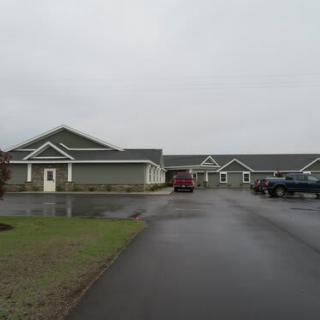A view of a building with a driveway and parked vehicles on an overcast day.