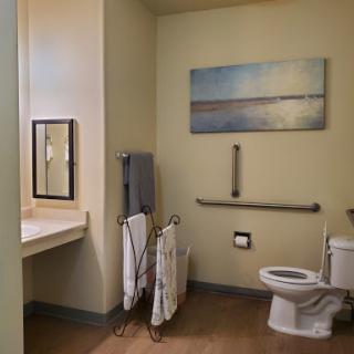 A clean and accessible bathroom featuring a toilet, sink, mirror, and towels.