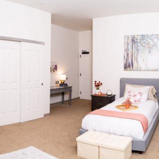 A minimalist bedroom with modern decor, featuring a single bed, nightstand, desk, and artwork on the wall.
