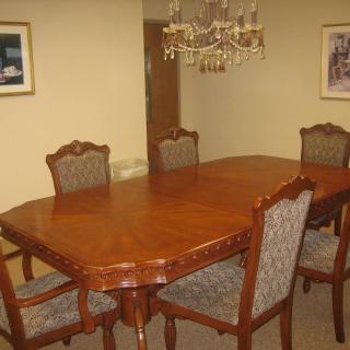 A dining room with a wooden table and cushioned chairs under an elegant chandelier.