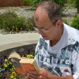A man reading a book while sitting outdoors in a garden.