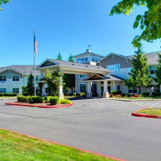 A large building with a landscaped entrance and driveway, featuring an American flag and surrounded by trees.