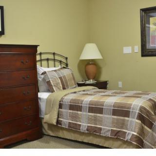 A cozy bedroom with a single bed, a wooden dresser, and a bedside lamp.