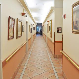 A brightly lit hallway with framed artwork on the walls and tiled flooring.