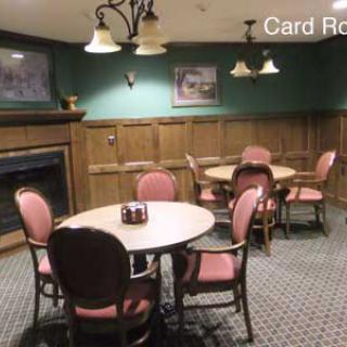 A cozy card room with round tables, chairs, and a fireplace.